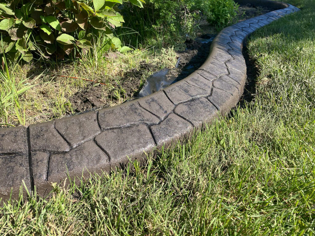 Curved concrete landscape edging with a stone-texture pattern separating a garden bed from the lawn.